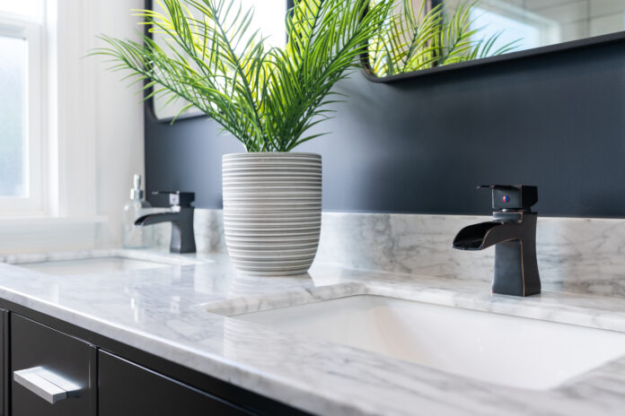 Detail of double bathroom sink with white and gray marble top and green potted plant. Profesjonalne aranżacje łazienki z marmurem